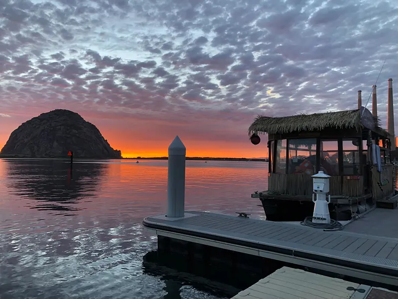 The Lost Isle Adventures tiki boat at the dock with Morro Rock at sunset
